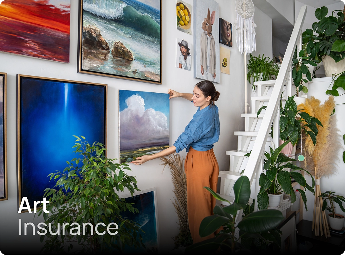 Woman hanging art on the wall of her home. Typical of what would be covered under art insurance.