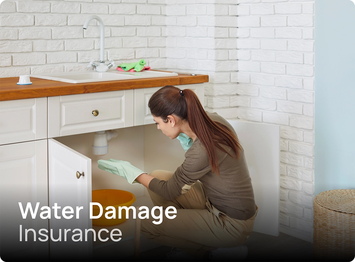 Woman on the phone while assessing a problem under the kitchen sink which may be covered by water damage insurance.